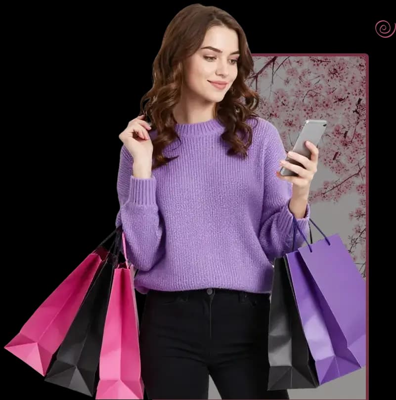 Woman in a purple sweater holding shopping bags in both hands while looking at a smartphone, standing in front of a pink cherry blossom background.